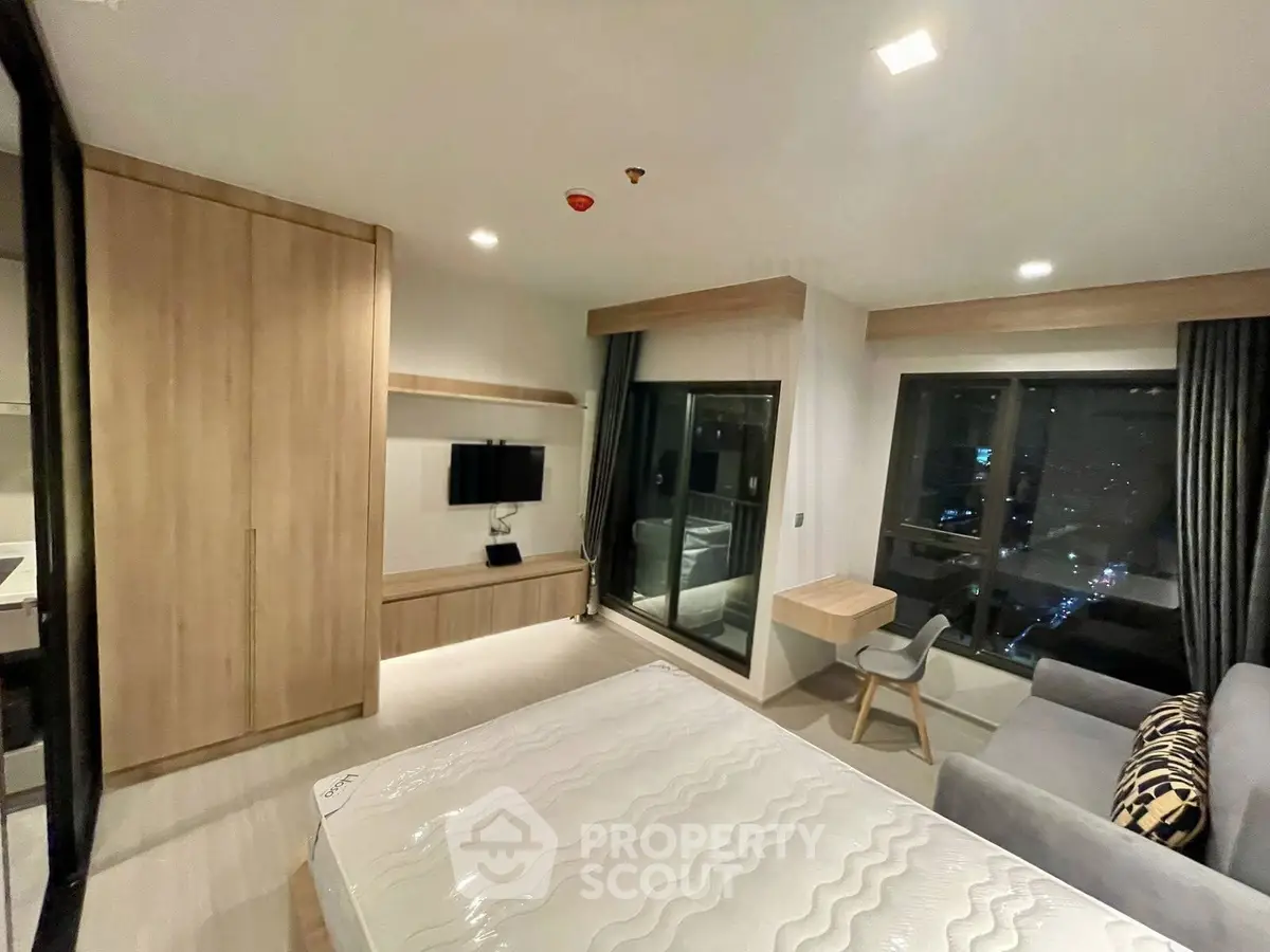 Modern bedroom with city view, featuring sleek furniture and large windows for natural light.