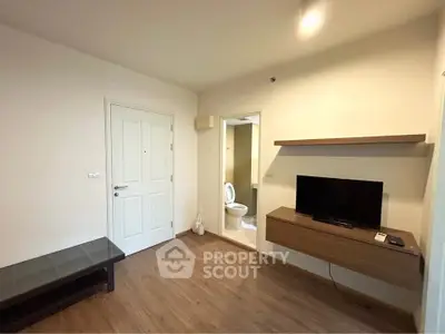 Modern living room with wooden flooring, wall-mounted TV, and adjacent bathroom entrance.