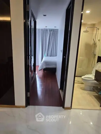 Modern apartment hallway leading to a cozy bedroom and sleek bathroom with glass shower.
