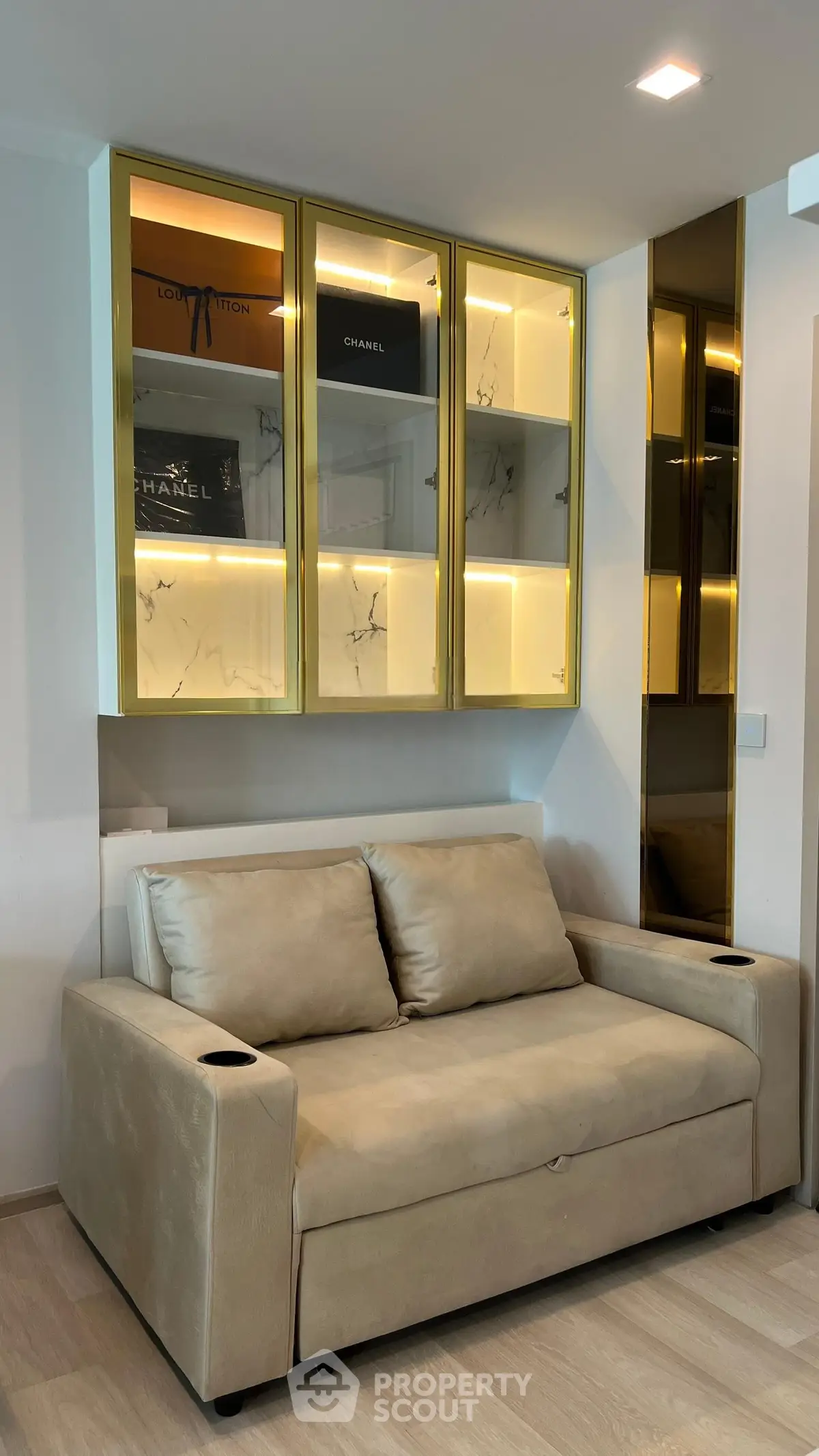 Luxurious living room with elegant beige sofa and illuminated glass cabinets showcasing designer items.