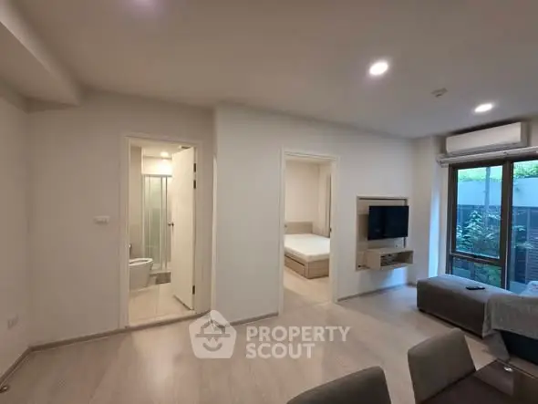 Modern living room with open layout and view into bedroom and bathroom, featuring sleek design and natural light.