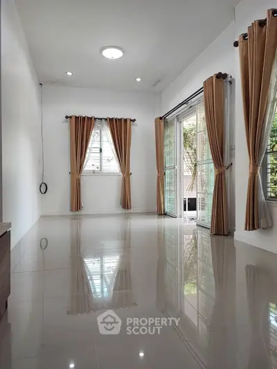 Spacious empty living room with glossy tiled floors and large windows with curtains.