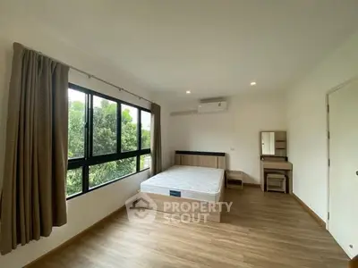 Spacious bedroom with large window and modern furnishings, offering a serene view of greenery.