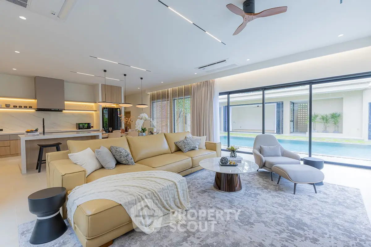Luxurious open-plan living room with modern kitchen and pool view, featuring elegant furniture and ample natural light.
