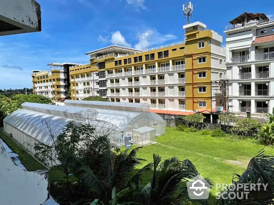 Modern apartment complex with lush green surroundings and greenhouse structures.