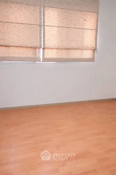 Spacious empty room with wooden flooring and large windows with blinds.