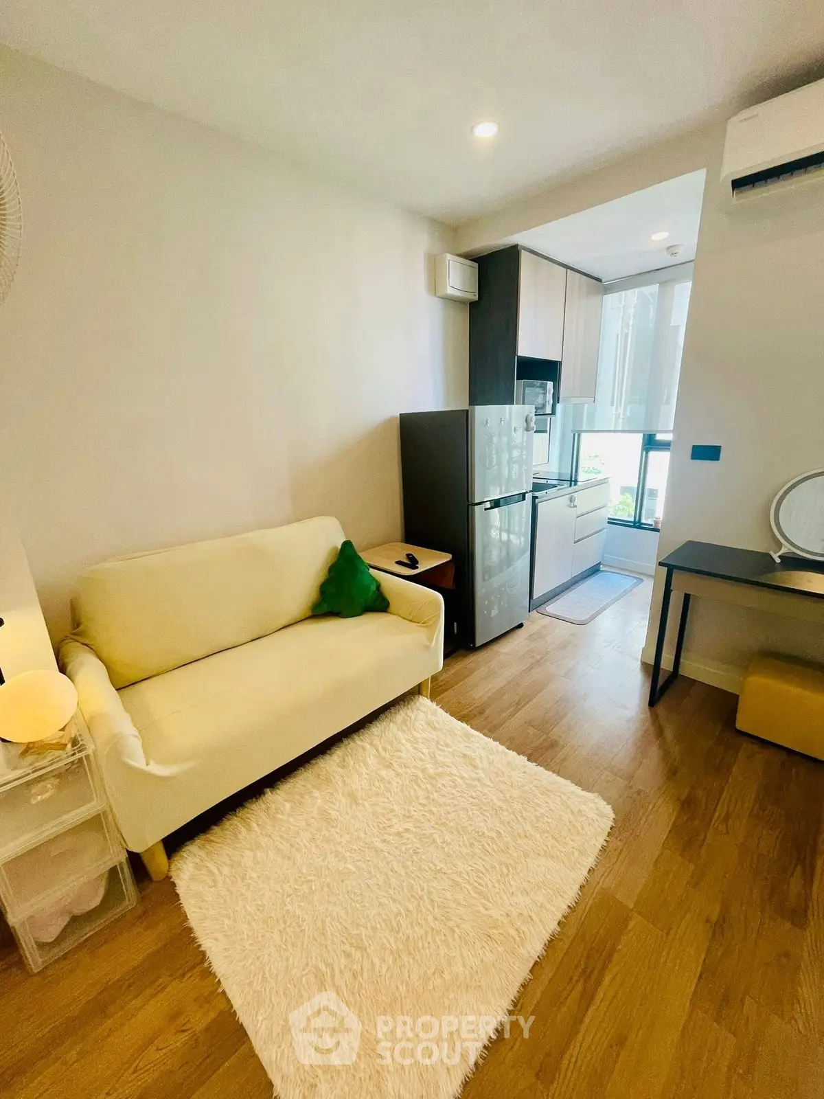 Cozy living room with modern kitchen in compact apartment, featuring wooden flooring and natural light.