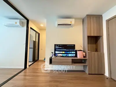 Modern living room with sleek wooden flooring, mirrored closet, and wall-mounted TV unit.