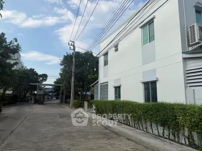 Modern white building exterior with lush greenery and clear blue sky.