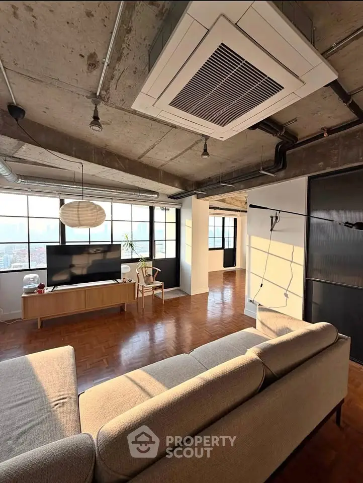 Spacious industrial-style living room with large windows and modern furnishings.