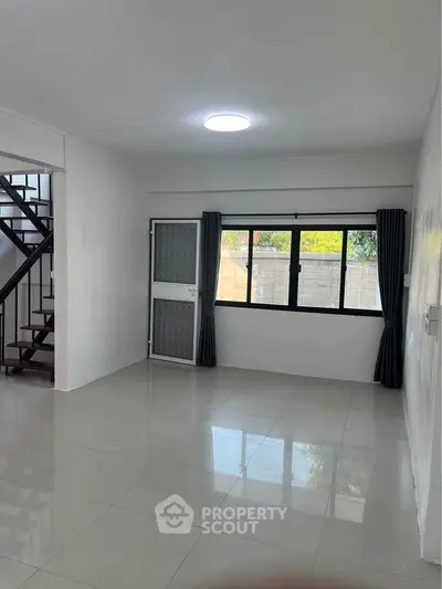 Spacious modern living room with large window and staircase, perfect for family gatherings.