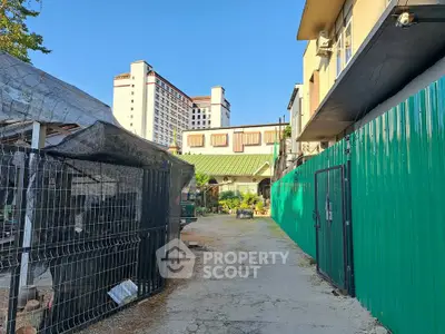 Charming urban alleyway with residential buildings and green fencing, perfect for city living.
