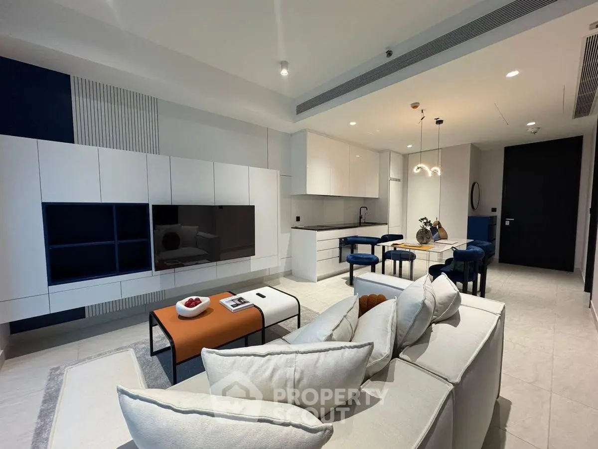 Modern living room with sleek design, featuring a large TV, stylish furniture, and open kitchen layout.
