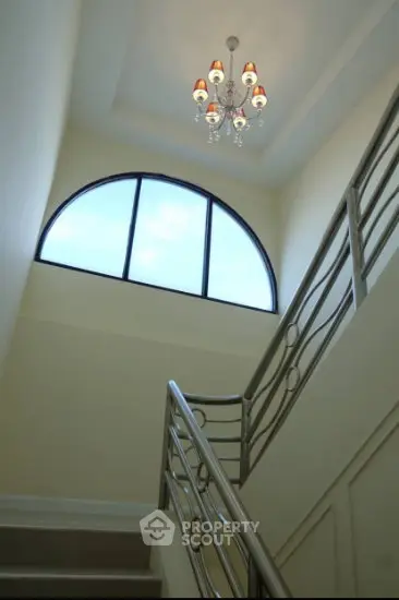 Elegant staircase with modern chandelier and large arched window