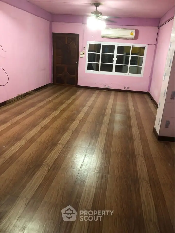 Spacious empty room with wooden flooring and pink walls, featuring a ceiling fan and air conditioning unit.