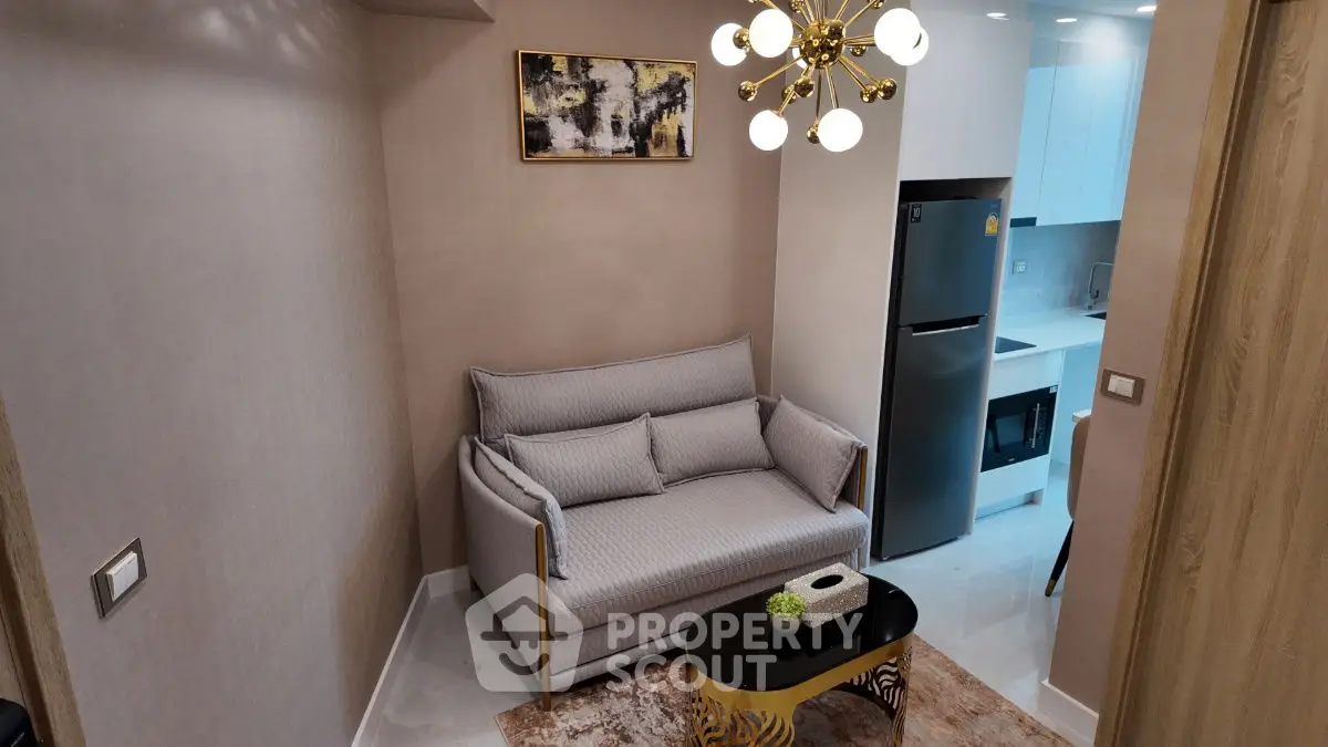 Modern compact living room with stylish sofa and chic lighting, adjacent to a sleek kitchen area.