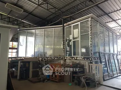Industrial warehouse interior with large glass enclosure and metal roof structure.