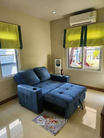 Cozy living room with blue recliner sofa and air conditioning, featuring large windows with green curtains.