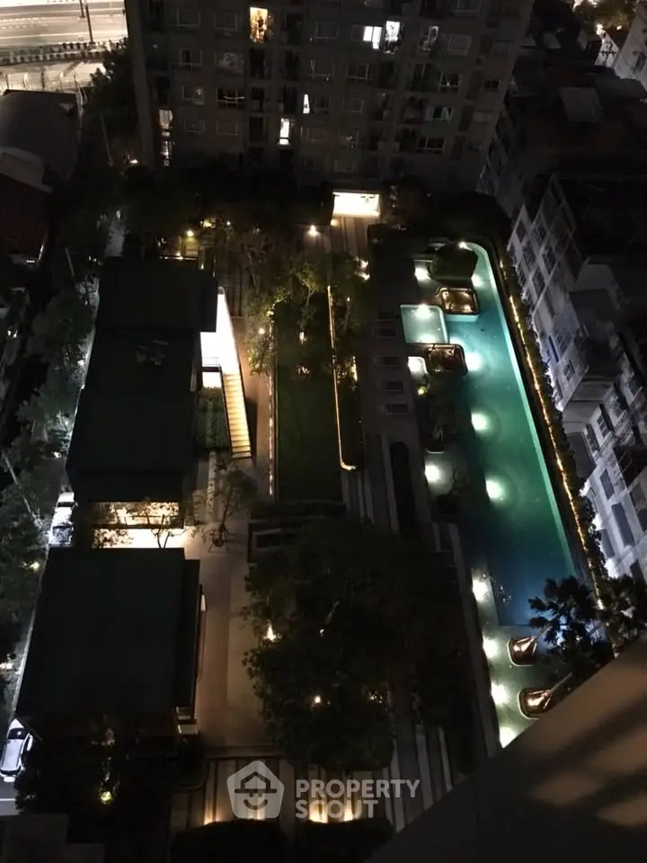 Stunning aerial view of illuminated modern apartment complex with pool and garden at night.