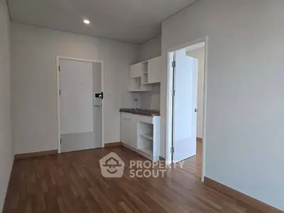 Modern minimalist apartment interior with wooden flooring and compact kitchen area.