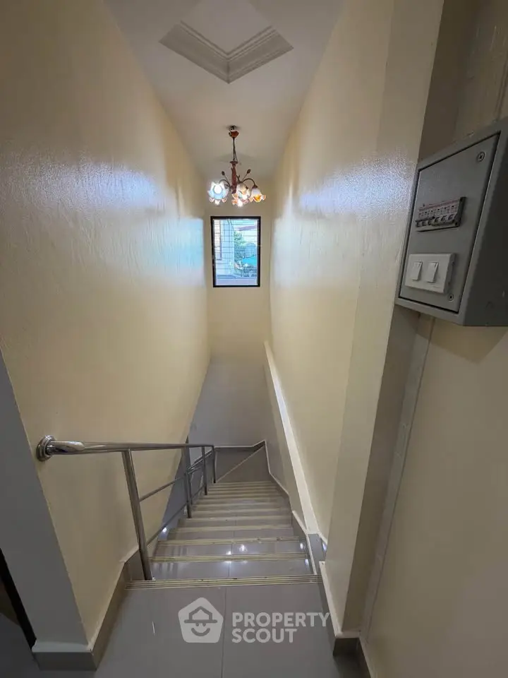 Elegant staircase with modern lighting in a residential building, featuring sleek handrails and a small window.