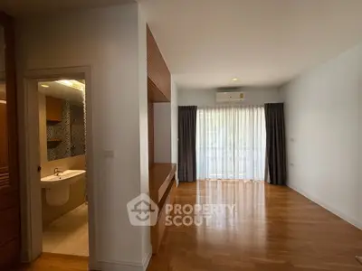 Spacious living room with wooden flooring and natural light, adjacent to a modern bathroom.