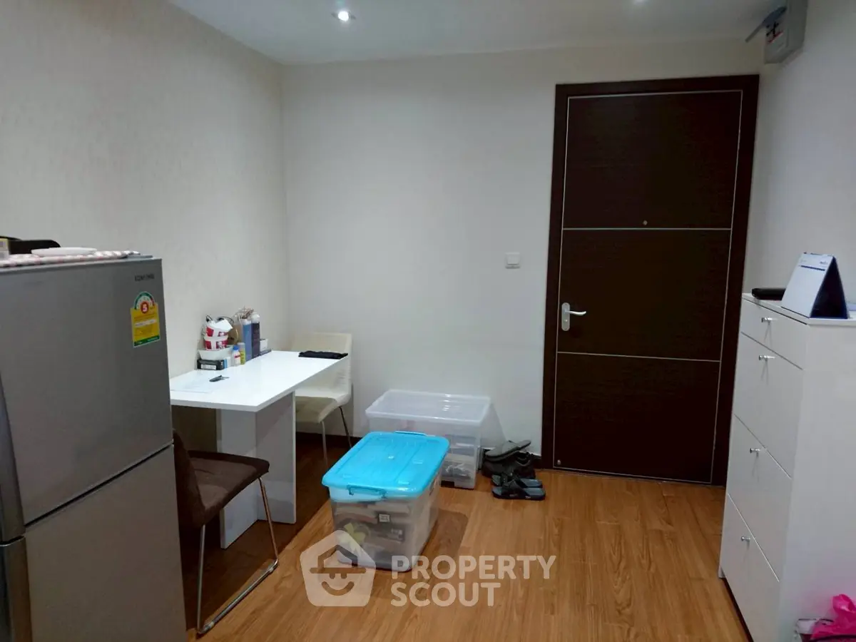 Compact interior with fridge, table, and storage boxes on wooden floor