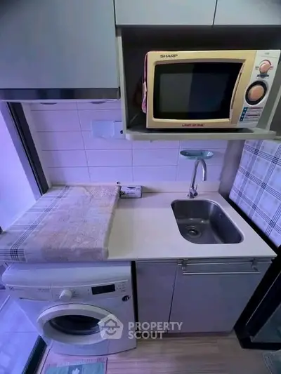 Compact kitchen with washing machine, microwave, and sink in modern apartment.