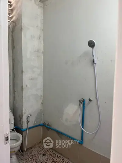 Basic bathroom with shower and toilet, featuring simple tile flooring and exposed plumbing.