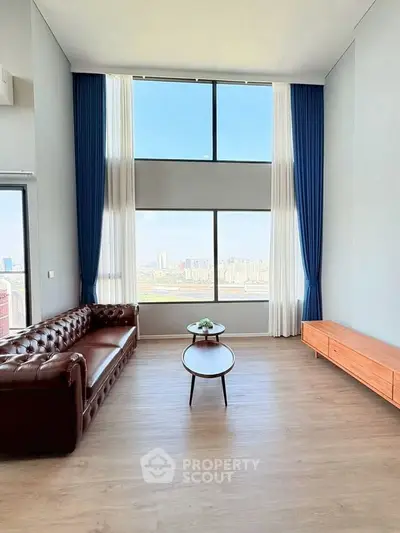 Spacious living room with high ceilings and stunning city view through large windows.