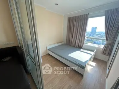 Bright bedroom with large window offering city view, featuring wooden flooring and modern furnishings.