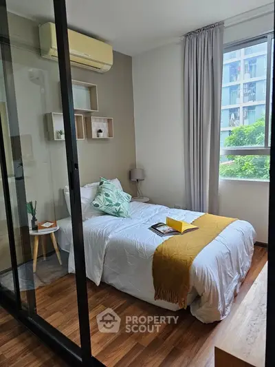 Cozy bedroom with modern decor and large window offering natural light and city view.