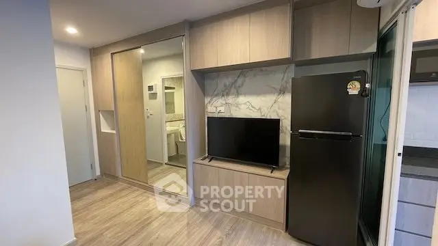 Modern apartment interior with sleek wooden cabinetry, mirrored wardrobe, and stainless steel fridge.