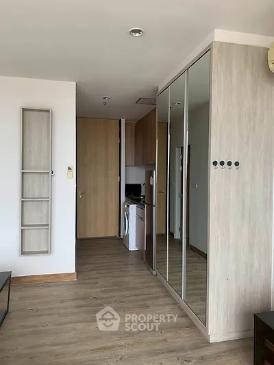 Modern apartment interior with mirrored closet and wooden flooring, featuring a compact kitchen area.