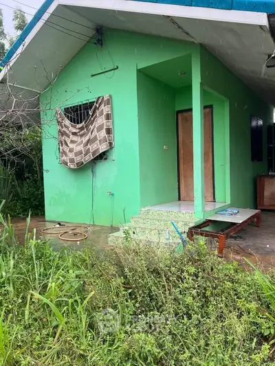 Charming green house with covered porch and lush garden, perfect for nature lovers seeking tranquility.