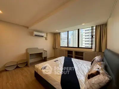 Spacious bedroom with modern furnishings and city view, featuring a comfortable bed and stylish desk.