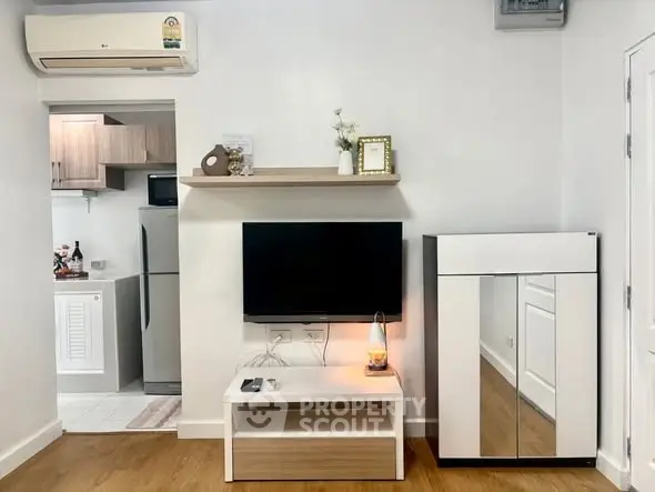 Modern living room with sleek TV setup and stylish decor, adjacent to a compact kitchen area.