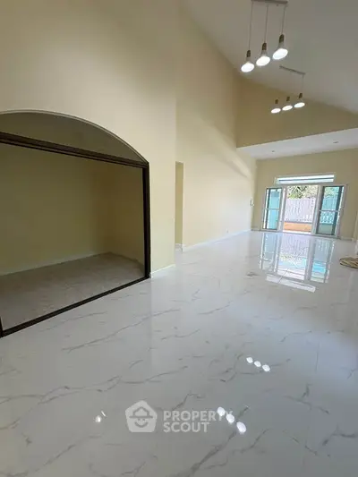 Spacious living room with high ceilings and elegant lighting, featuring glossy marble floors and large windows.