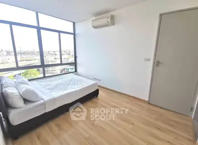 Spacious bedroom with large windows and city view, featuring modern air conditioning and sleek wooden flooring.