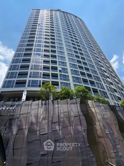 Stunning modern high-rise building with sleek glass facade and lush greenery at the base.
