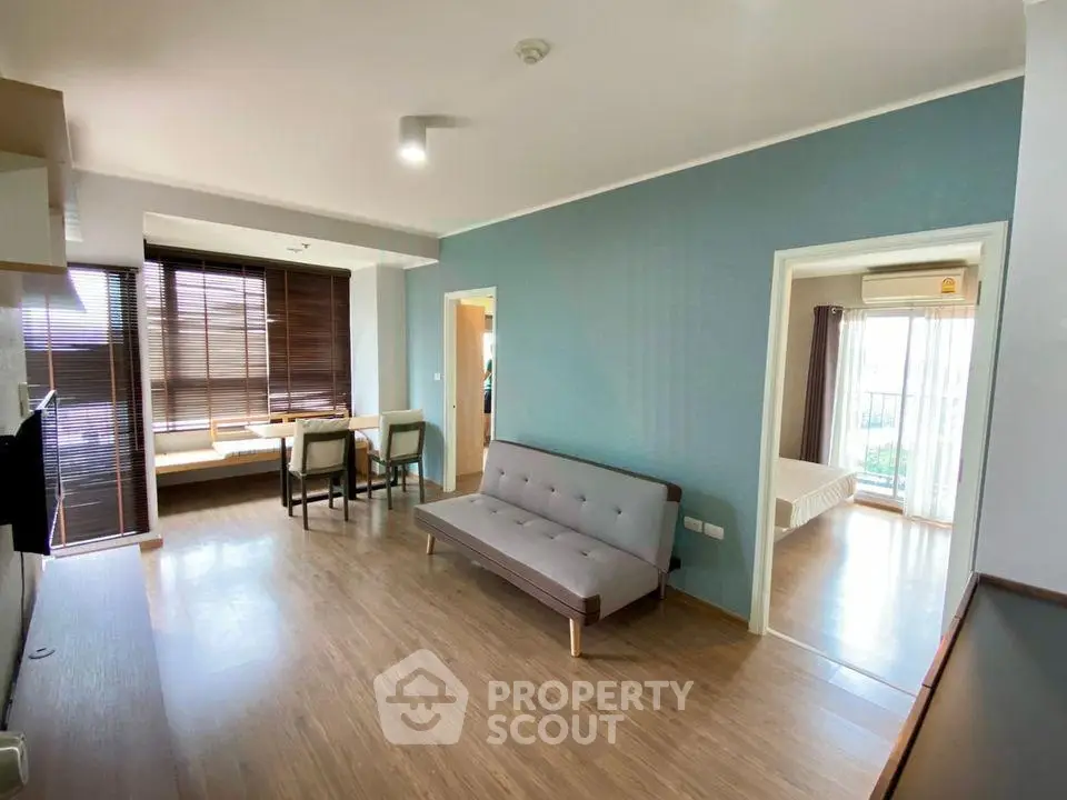 Spacious modern living room with wooden flooring and natural light, adjacent to a cozy bedroom.