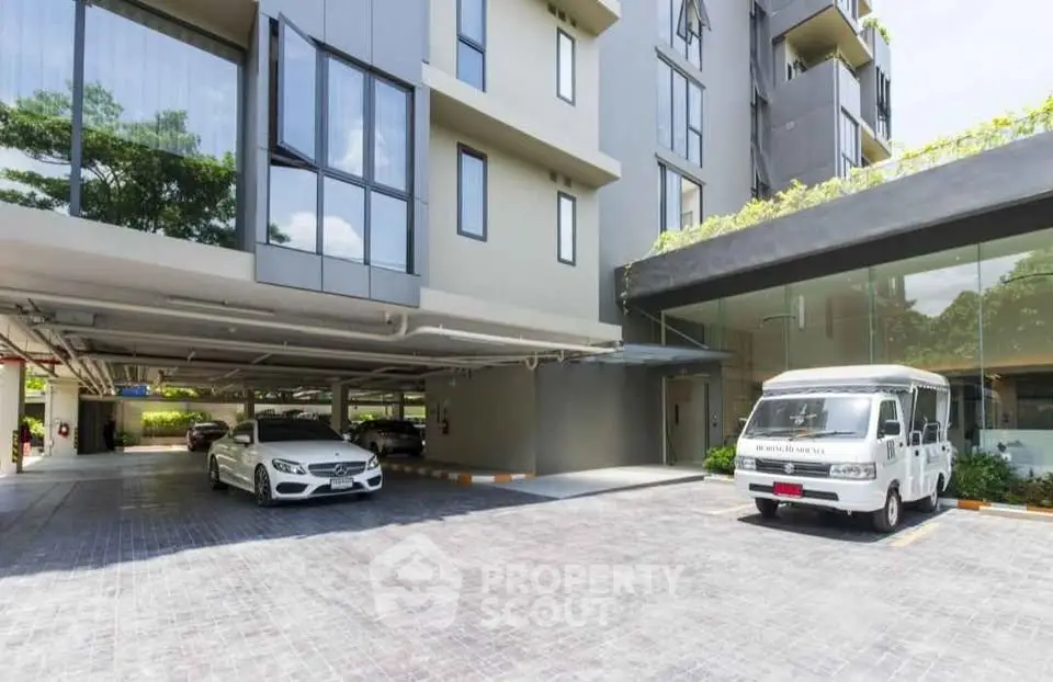 Modern apartment building with parking area and sleek glass facade.