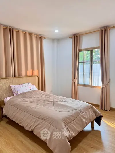 Cozy bedroom with natural light, wooden flooring, and elegant curtains, perfect for relaxation.