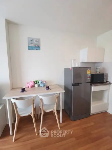 Cozy kitchen nook with dining table, chairs, fridge, and microwave in modern apartment.