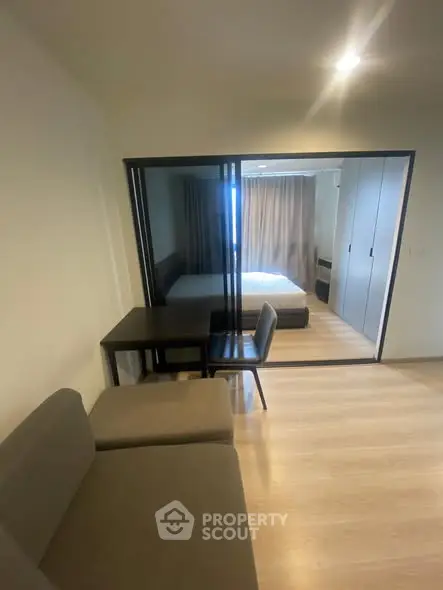 Modern apartment interior with cozy living area and view into bedroom through glass partition.