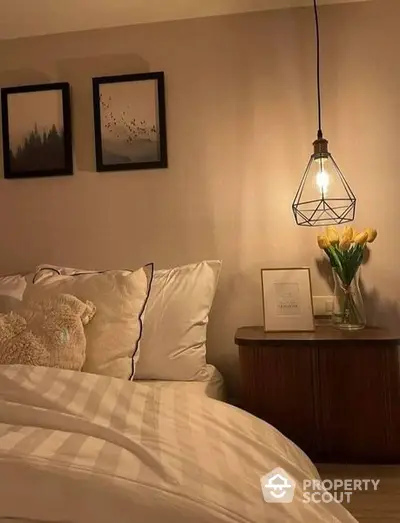 Cozy bedroom corner with stylish bedding, elegant side table, fresh flowers, and unique pendant light, perfect for a restful retreat.