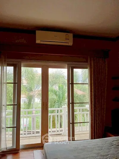 Spacious bedroom with balcony and lush garden view, featuring large windows and air conditioning.