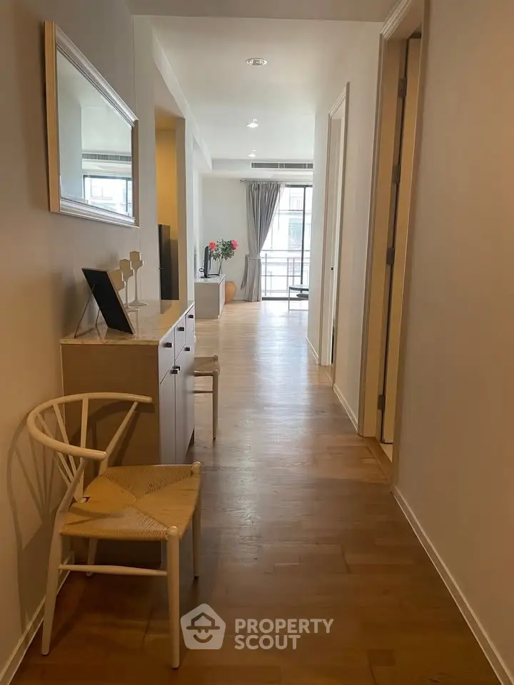 Bright hallway with wooden flooring leading to a living area with large windows and modern decor.