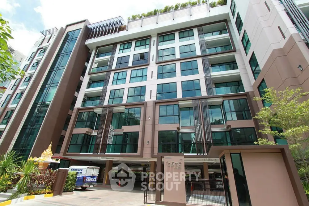 Modern multi-story residential building with large windows and lush greenery.