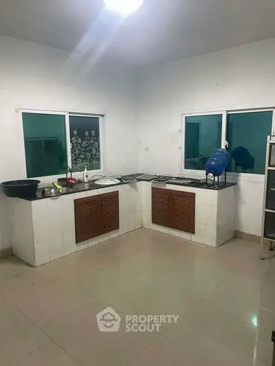 Spacious kitchen with tiled flooring and ample counter space, featuring large windows for natural light.